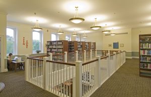 several rows of bookshelves on the Community Library's 2nd floor beside the open balcony looking down to the 1st floor