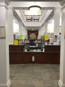 the main circulation desk centered between two square pillars inside the front entrance of the community library