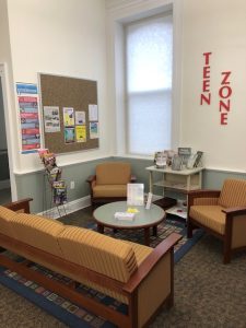 the library's teen zone with two arm chairs and a couch, a table and a bulletin board