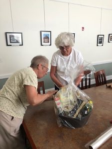 two female volunteers wrap a gift basket in cellophane in preparation for the basket raffle